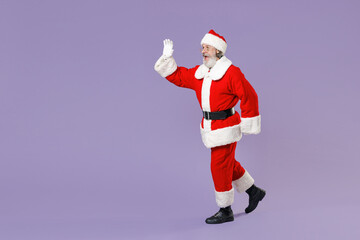 Full length side view portrait amazed Santa Claus man in Christmas hat suit waving greeting with hand as notices someone isolated on violet background Happy New Year celebration merry holiday concept.