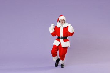 Full length portrait of Santa Claus man in Christmas hat red suit coat white gloves glasses clenching fists like winner isolated on violet background. Happy New Year celebration merry holiday concept.