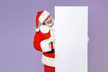 Cheerful Santa Claus man in Christmas hat red coat suit gloves glasses hold big white empty blank billboard isolated on violet background in studio. Happy New Year celebration merry holiday concept.