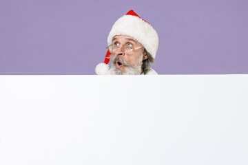 Shocked amazed Santa Claus man in Christmas hat red coat gloves glasses hold big white empty blank billboard isolated on violet background studio. Happy New Year celebration merry holiday concept.
