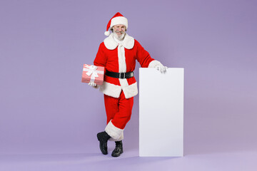 Full length portrait Santa Claus man in Christmas hat suit hold big white empty blank billboard present box with gift ribbon isolated on violet background. Happy New Year celebration holiday concept.