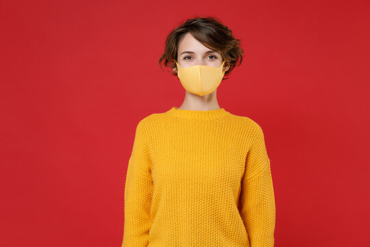Young brunette woman 20s wearing casual yellow sweater face mask to safe from coronavirus virus covid-19 during pandemic quarantine looking camera isolated on bright red background studio portrait. - Powered by Adobe