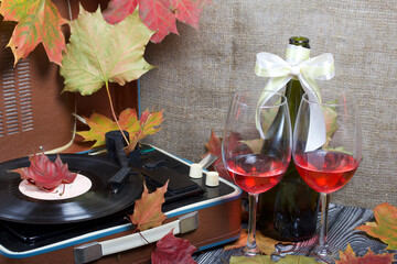 Old turntable. Scattered with autumn maple leaves. Nearby are two glasses and a bottle of alcohol. Retro party equipment.