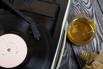 Old turntable. Nearby is a flask and a glass of strong alcohol. Retro party equipment.