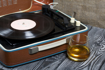 Old turntable. Nearby is a glass of strong alcohol. Retro party equipment.