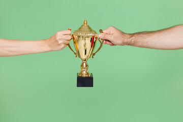 Close up cropped of two male female hands horizontal holding football winner cup isolated on green background. Sport fans cheer up. Friends leisure lifestyle concept.