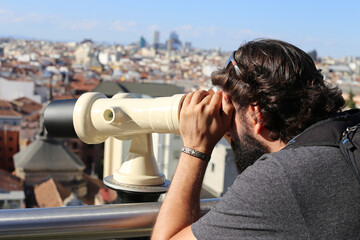 Fototapeta na wymiar Selective focus shot of an handsome caucasian male admiring Madrid through a telescope
