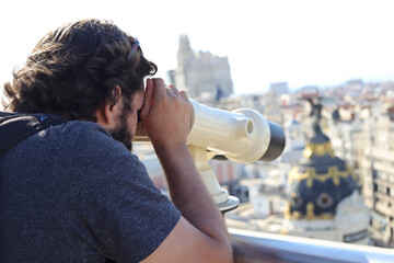 Selective focus shot of an handsome caucasian male admiring Madrid through a telescope