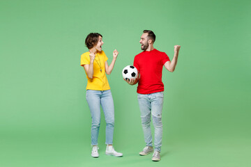 Fototapeta na wymiar Full length of excited young couple friends sport family woman man football fans in t-shirts cheer up support favorite team with soccer ball clenching fists like winner isolated on green background.