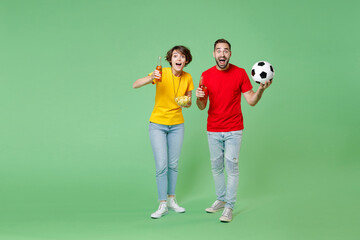 Full length excited young couple friends sport family woman man football fans in t-shirts cheer up support favorite team with soccer ball hold beer bottles chips isolated on green background studio.