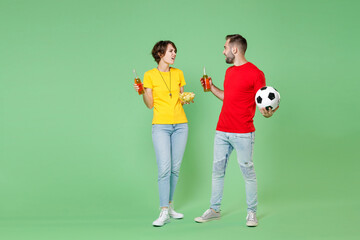 Fototapeta na wymiar Full length displeased young couple friends sport family woman man football fans in t-shirts cheer up support favorite team with soccer ball hold beer bottles chips isolated on green background studio