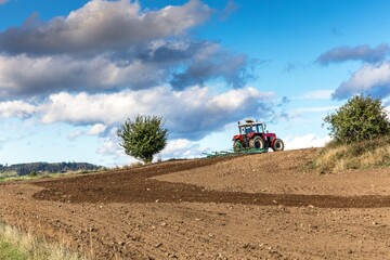 Red tractor cultivates the soil in the field with a cultivator after harvest. Autumn sunny day.  Agricultural landscape in the Czech Republic. Work on the farm.