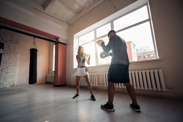A man and a woman sparring partners train in the fighters training hall in boxing gloves with paws