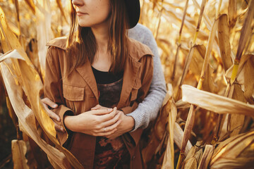 Young man gently hugging his fashionable woman in autumn corn field, touch close up