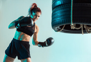 A female fighter in Boxing gloves strikes the tires with her hand