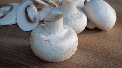 Bright white mushrooms, both sliced and whole, in great close up on a wooden cutting board. Spectacular details are visible in this isolated macro photo of the mushroom. Food and culinary concept.
