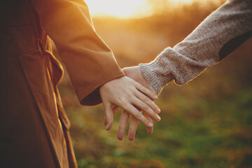 Couple gently holding hands in warm sunset light in autumn field, close up. Conceptual image