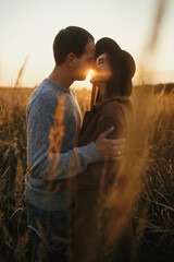 Stylish sensual couple embracing in warm sunset light in autumn field, gently hugging in sunshine