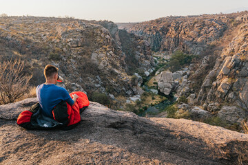 young drinking tea, over sleeping bag on top of mountains. Adventurer drinking coffee at the top. Camp in mountain landscape