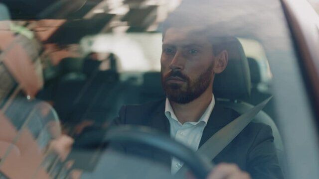Portrait young confident man driving sitting in the car at sunset. Look around serious. Automobile work city. Driver businessman beard travel. Slow motion