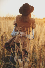 Stylish happy couple dancing in sunset light in autumn field, twirling among grass in sunshine