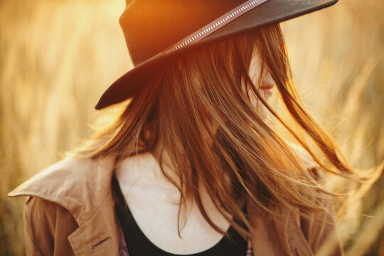 Portrait of boho woman in hat with windy hair in sunset light in autumn field, carefree moment