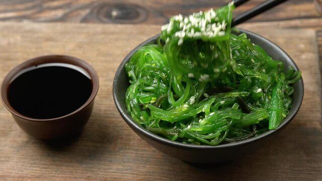Eating of tasty seaweed salad from bowl on table