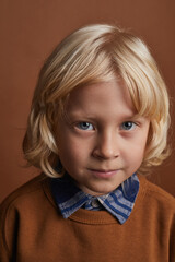 Portrait of little boy with long blonde hair looking at camera against the brown background