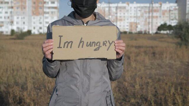 Pandemic, hunger. Without work during epidemic. A woman in a protective mask holding a sign I AM HUNGRY.
