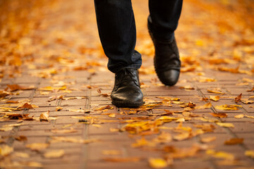 Men boots walking on the sidewalk strewn with autumn leaves