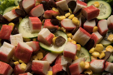 Healthy food and nutrition. Closeup view of a fresh salad dish with corn grains, lettuce, cucumber, black olives and crab sticks, on the wooden table.