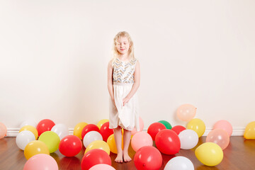 Fototapeta na wymiar Cute adorable girl in white dress celebrating birthday at home. Lovely girl child having fun with colorful balloons. Quarantine birthday party at home alone. Social distance, self-isolation.