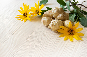 flowers and roots of the Jerusalem artichoke plant lie on a light wooden background