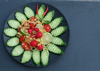 Mango salad with lime and peanuts in black plate on black slate.