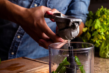 Man squeezing lime with a metal squeezer into a bowl.