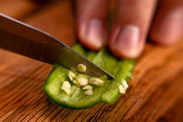Hands unveiling a serrano pepper with a knife to prepare a mexican dish. Close up of seeds.