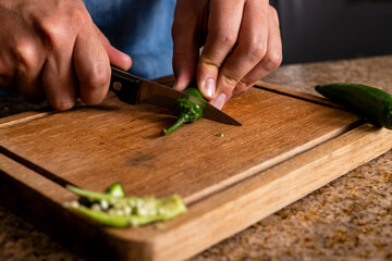Hands unveiling a serrano pepper with a knife to prepare a mexican dish.