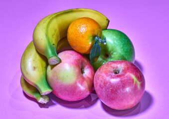Bananas, apples and tangerines on branch on lilac background