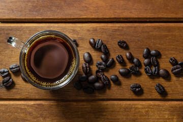 Xícara de café e grãos espalhados sobre a mesa de madeira. © Angela