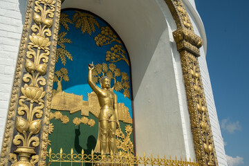 A golden statue of Buddha, standing with a raised hand, located in a niche, surrounded by traditional Buddhist designs