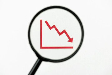 MAGNIFIER ON DESCENDING ECONOMIC GRAPHIC. ECONOMY MONITORING. CRISIS CONCEPT.
