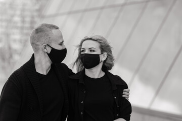 Couple wearing fashionable protective masks, walking in empty street of city during quarantine.