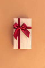 Gift in a box with dark red bow on beige background, top view