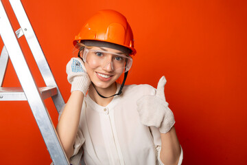 beautiful young woman in hard hat near stepladder on red background with hand gesture