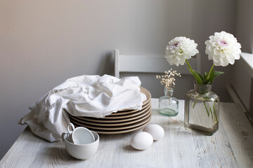 Two white dahlia flowers in a pharmaceutical bottle instead of a vase. Wooden box for storing bottles with decorative small bottles in the grey kitchen.