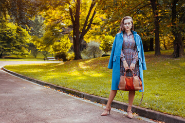 Obraz premium Full body portrait of stylish young woman walking in park with handbag wearing trendy outfit. Autumn fashion