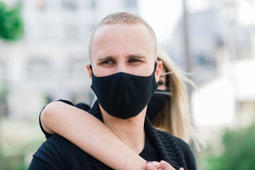 Couple wearing fashionable protective masks, walking in empty street of city during quarantine.