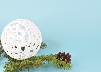 Knitted Christmas ball-shaped toy lying on a spruce branch next to a pine cone.