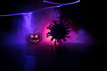 Halloween during Corona virus global pandemic concept. Glowing pumpkins and Covid novel on dark with thematic spooky decorations. Halloween pumpkin on foggy backlight.