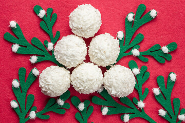 round candies sprinkled with coconut flakes on a red background with felt green sprigs